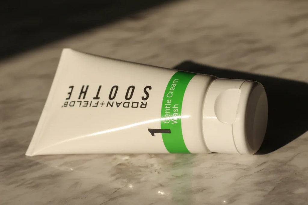 Close-up macro of Rodan + Fields SOOTHE Gentle Cream Wash tube with green accent band in soft morning light