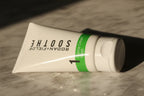 Close-up macro of Rodan + Fields SOOTHE Gentle Cream Wash tube with green accent band in soft morning light