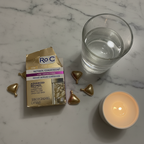 RoC Retinol Correxion Night Serum Capsules on white marble vanity with candle and glass of water.
