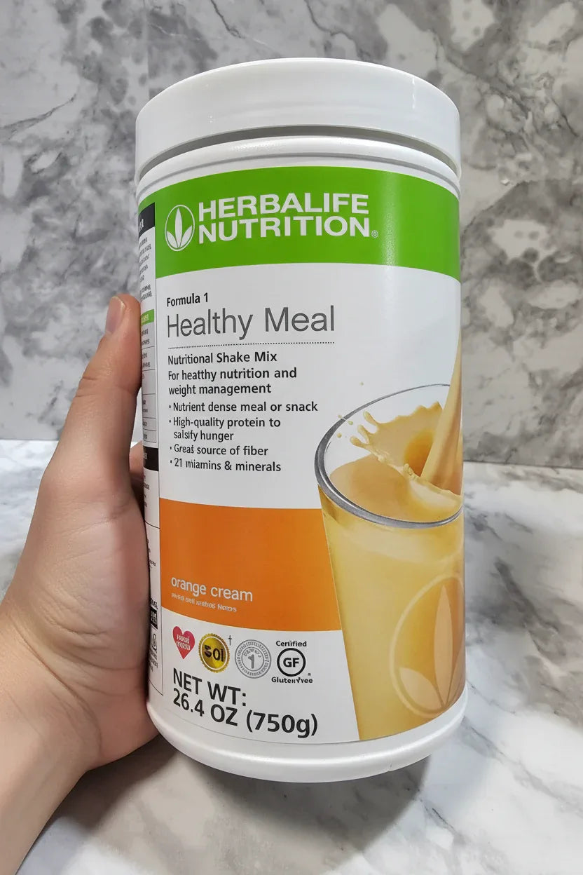 In-hand close-up of Herbalife Formula 1 Orange Cream canister on white marble surface