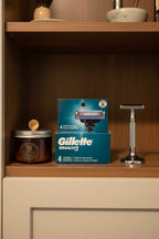 Gillette Mach3 4-pack razor refills on wooden shelf in grooming cabinet with shaving soap and chrome stand