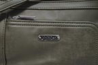 Close-up of MultiSac Summerville olive green vegan leather crossbody bag silver logo plate and zipper hardware detail