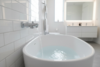 Grohe Lineare StarLight chrome tub spout with pull diverter wall mounted on white subway tile above freestanding soaking tub with water flowing