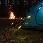 TentBrightz LED lights clipped to tent guylines glowing at night with campfire in background.