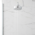 Grohe Tempesta Cosmopolitan 100 polished chrome shower head mounted on a white marble tile shower wall with water streaming.