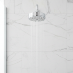 Grohe Tempesta Cosmopolitan 100 polished chrome shower head mounted on a white marble tile shower wall with water streaming.