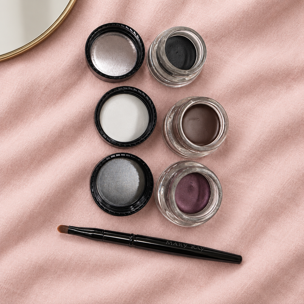 Flat lay of three open Mary Kay Gel Eyeliner pots and Mary Kay brush on pink linen