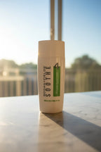 Soft morning sunlight hitting a minimalist white skincare bottle near a bright bathroom window on white marble