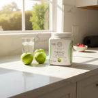 Sunwarrior Thermo Greens tub in vibrant morning kitchen with fresh green apples, glass of water, and sunlight.