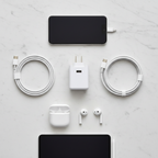 Flat lay of white USB-C charger block with coiled white cables and mobile devices on white marble