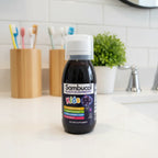 Sambucol Kids Black Elderberry Syrup 4oz bottle on white quartz family bathroom vanity with wooden toothbrush holder and fresh green houseplant