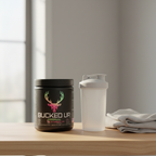 Bucked Up Original Strawberry Kiwi pre-workout container on a home gym shelf beside a shaker bottle and towel
