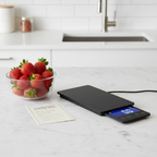 Lifestyle — slim black digital food scale with pull-out display on white marble counter beside glass bowl of strawberries and recipe card — clean modern kitchen flatlay editorial for visual context only
