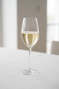 Sparkling Prosecco with rising bubbles in a tall elegant Riedel crystal champagne glass on white linen tablecloth