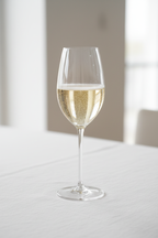 Sparkling Prosecco with rising bubbles in a tall elegant Riedel crystal champagne glass on white linen tablecloth