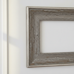 Close-up of a weathered grey picture frame with silver-tone trim on a white wall