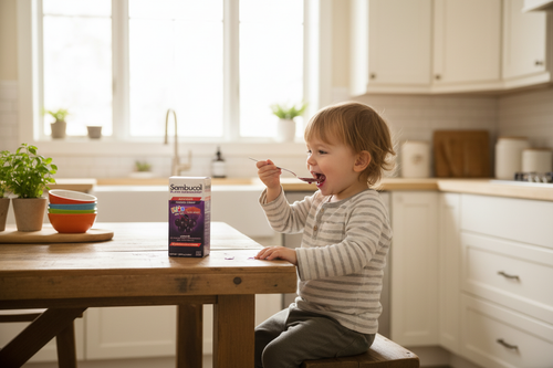 Happy young child taking a spoonful of purple berry syrup from a parent's hand in a bright kitchen