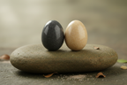 Two smooth oval sensory fidget stones resting elegantly on a natural flat river stone surface with soft diffused light