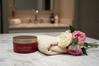 Luxury red body cream jar with gold lid on marble surface next to fresh flowers