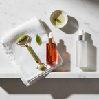 Lifestyle image - red glass serum bottle beside jade roller and linen towel on bathroom shelf, morning skincare routine editorial for visual context only