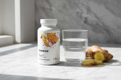 Thorne supplement bottle on marble surface next to glass of water and fresh ginger root