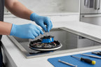 Stainless steel electric cooktop being serviced by hand with precision tools