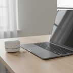Small white circular mini desktop vacuum on a tidy modern home office desk next to a laptop keyboard with eraser crumbs nearby