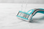 Water droplets splashing gently against a high-quality 5-blade women's razor cartridge on white marble