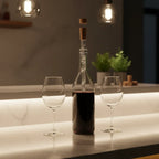 Kitchen counter bar display with wine bottle featuring Corkcicle Air chiller aerator beside wine glasses, warm ambient lighting