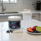 Alani Nu Cosmic Stardust Pre-Workout tub on kitchen workspace with shaker bottle and fresh fruit.