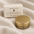 AI-generated lifestyle photo of the Mary Kay Satin Lips Lip Balm jar and retail box on soft fabric