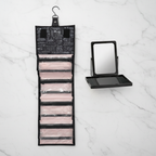 Flat lay overhead of the Mary Kay roll-up travel bag unrolled with all four compartments and the Face Case Mirror on a white marble surface.