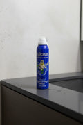 Blue aerosol bottle sitting on a minimalist dark slate bathroom vanity in soft clean lighting