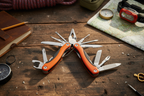 Adventure Is Out There 11-in-1 orange multi-tool fully deployed showing pliers, saw, knife and screwdrivers on wooden surface