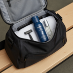 Men's grooming essentials with navy blue skincare bottle and razor neatly arranged in a modern gym bag