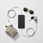Flat-lay road trip essentials with smartphone, white braided USB-C cables, sunglasses, and car keys on white surface