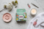 Flatlay of Gillette Venus Comfortglide Sugarberry Rifle Paper Co. box with pink vanity accessories, floral sprig, and white candle on marble surface