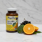 MegaFood Men's 40+ One Daily amber glass bottle beside fresh organic oranges broccoli and elderberries on white marble – More4less Outlet