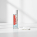 Rodan + Fields ESSENTIALS eye makeup remover bottle beside plain white cotton rounds on a clean vanity