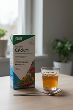 Salus Floradix Calcium Liquid Mineral Formula 250ml box on a light wood surface next to a small glass of liquid supplement and a spoon in a morning wellness setting – More4less Outlet