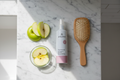 Arbonne TrueSmooth Apple Vinegar Hair Rinse spray bottle on marble vanity with hairbrush and fresh apple slices – More4less Outlet
