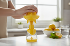 Person squeezing lemon with Core Kitchen yellow citrus juicer into clear measuring base — built-in strainer catches seeds for clean fresh juice