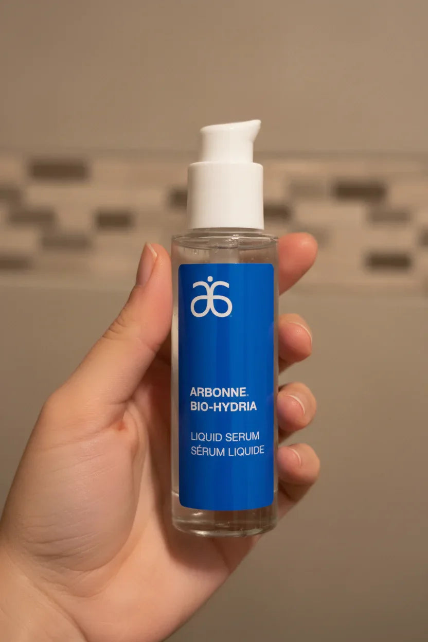 Arbonne Bio-Hydria Liquid Serum in-hand close-up neutral bathroom tile background