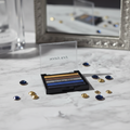 Mary Kay Eye Color Palette Rock the Runway open compact on a white marble vanity showing five metallic eyeshadow strips — gold, bronze, silver, cobalt blue, midnight navy — with dramatic studio lighting, blurred mirror, and scattered gold and navy gemstones