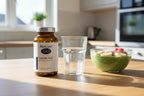 BioCare Caprylic Acid 90ct amber glass bottle on light wood breakfast bar with water and smoothie bowl — daily wellness supplement morning routine