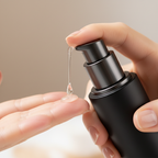 Hand pressing pump of clear lightweight Vitamin K serum onto fingertips from black skincare pump bottle – close-up texture shot
