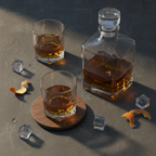 Flat lay of two crystal whisky glasses and a decanter on dark slate with warm lighting