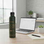 Matte dark green Akvati 32 oz water bottle on a wooden desk next to a laptop, notebook, and succulent plant in a modern home office.