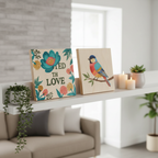 Two finished 8x8 inch painted wood panel home decor pieces displayed on a white shelf in a modern living room surrounded by small plants and candles.