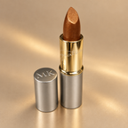 Mary Kay Gold Dust golden bronze lipstick on a warm champagne background
